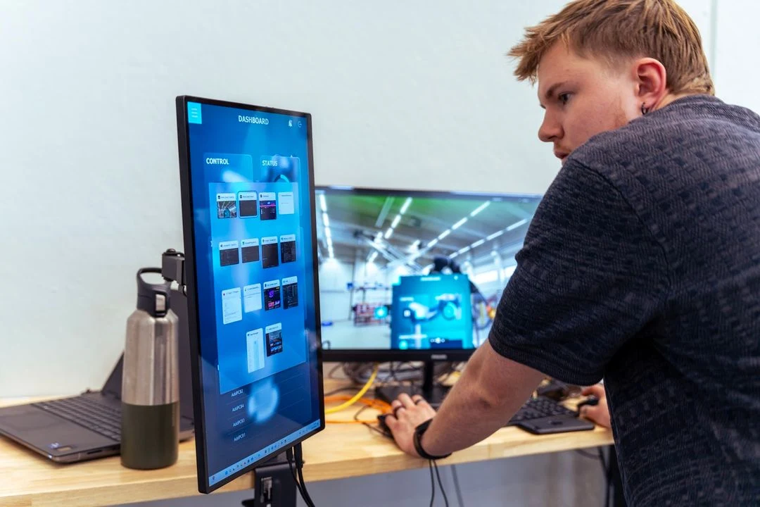 Engineer van Invisto test een dashboardapplicatie op een verticaal touchscherm, naast een monitor met een camerabeeld van een machine