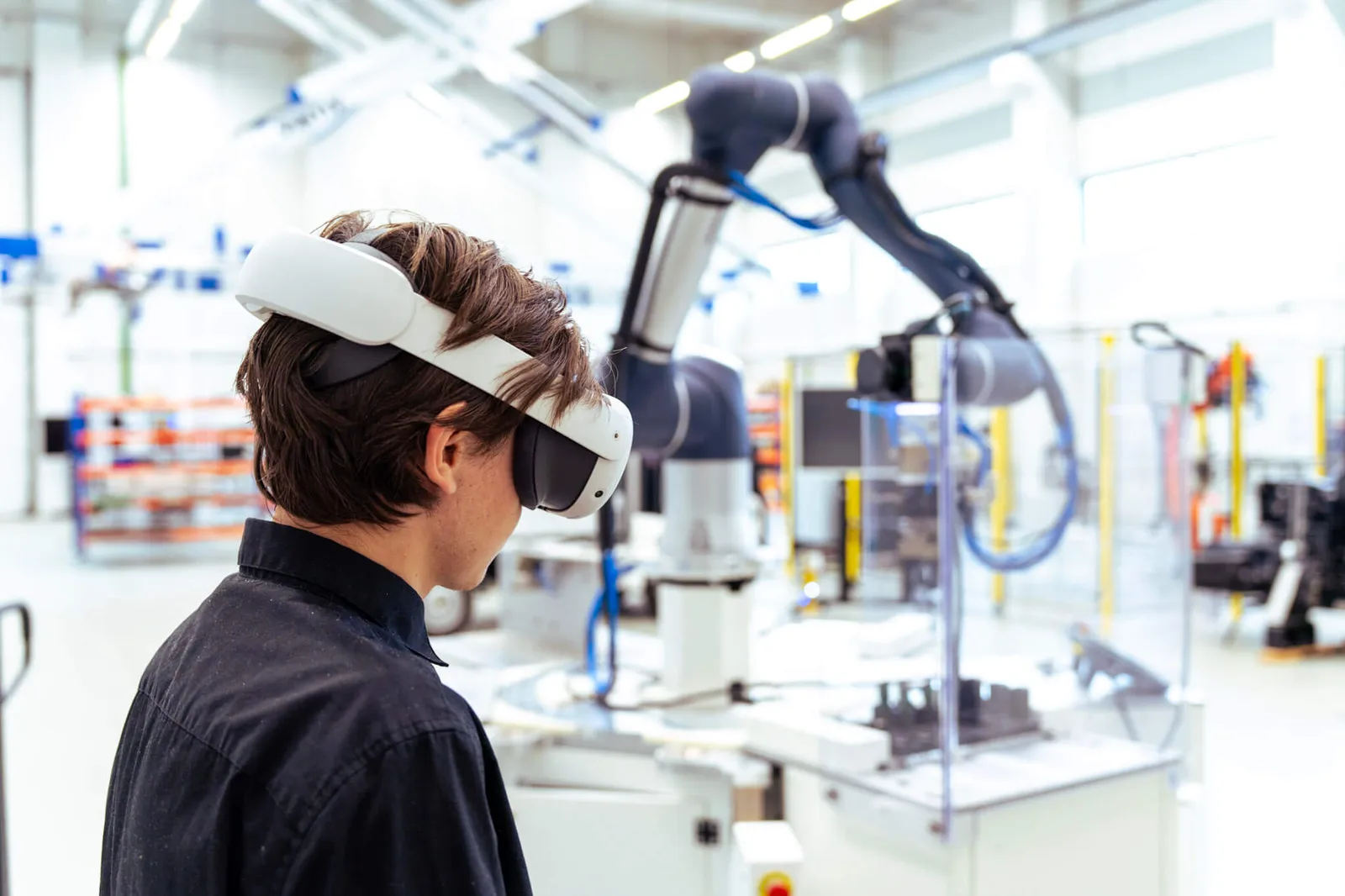 Employee wearing a VR headset next to a collaborative robot arm on a factory floor